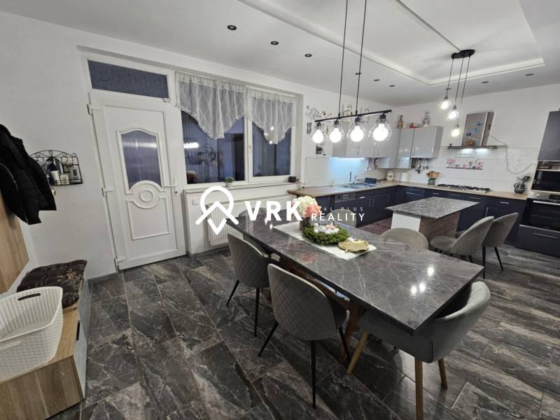 Jídelní prostor s kamenným stolem, šedými židlemi a závěsnými světly v rodinném domě.