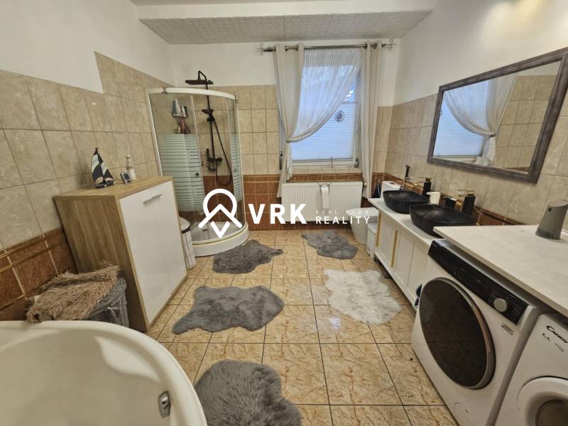Koupelna v rodinném domě s vanou, sprchovým koutem a pračkou.
