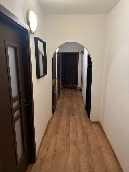 Úzká chodba v 2-pokojovém bytě s podlahou s dřevěným dekorem a tmavými dveřmi.