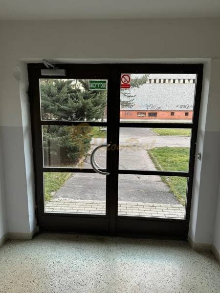 Skleněné vchodové dveře z interiéru, východ vede k upravenému trávníku a chodníku.