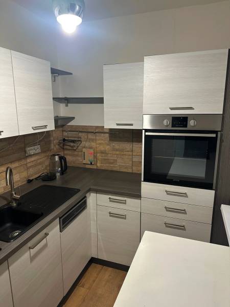 Kuchyň v 2-pokojovém bytě, s podlahou s dřevěným dekorem a vestavnou troubou.