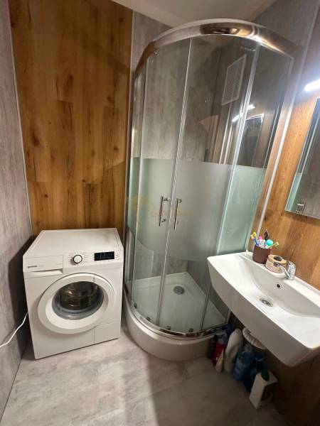 Koupelna v 2-pokojovém bytě s pračkou, sprchovým koutem a umyvadlem, dřevěný dekor stěn.