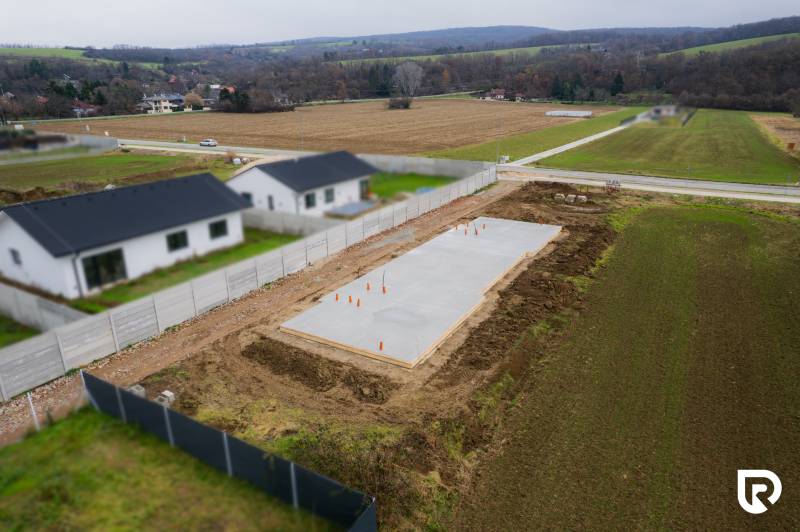 Základy rodinného domu v Sokolovcích, obklopené poli a sousedními domy.
