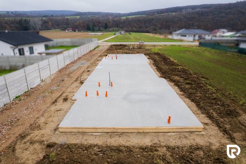 Základy rodinného domu v Sokolovcích obklopené venkovskou krajinou a sousedními domy.