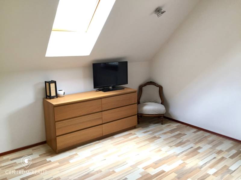 Interiér rodinného domu s komodou, křeslem a podlahou s dřevěným dekorem.