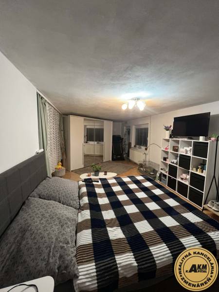 Ložnice v rodinném domě s manželskou postelí, bílým nábytkem a vzorovanou přikrývkou.