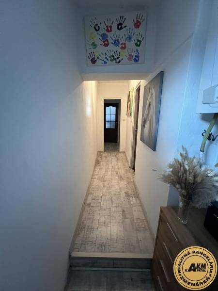 Úzká chodba v rodinném domě s dekorací dětských rukou a podlahou s dřevěným dekorem.