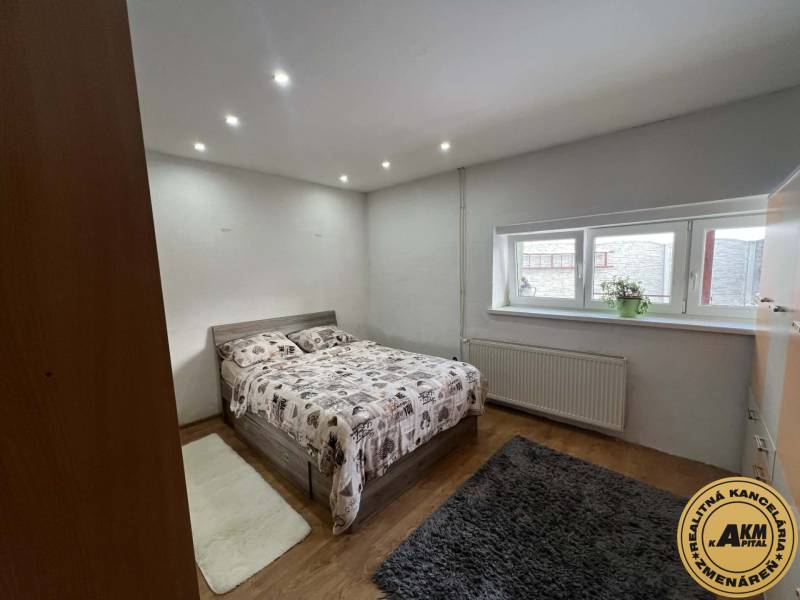 Ložnice v rodinném domě s postelí, oknem a podlahou s dřevěným dekorem.