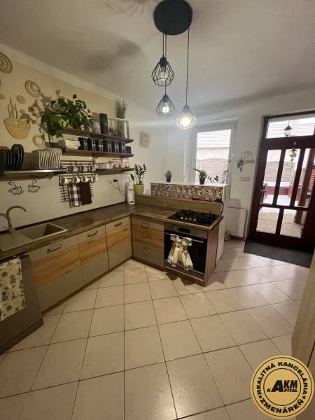 Kuchyně v rodinném domě s keramickou dlažbou, dřevěnými dekoracemi a otevřenými policemi.