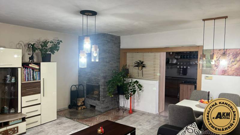 Interiér rodinného domu s krbem, závěsnými svítidly a podlahou s dřevěným dekorem.