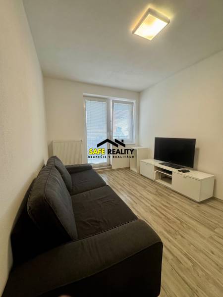 Obývací pokoj v 2pokojovém bytě s pohovkou, televizí a podlahou s dřevěným dekorem.