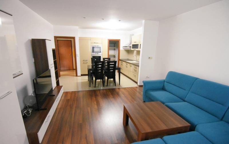 Obývací pokoj dvoupokojového bytu s podlahou s dřevěným dekorem a modrou sedačkou.