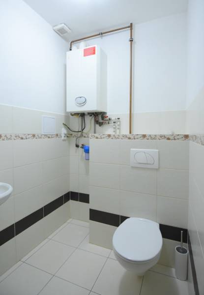 Koupelna v 2-pokojovém bytě s kotlem a toaletou, obložená keramickými dlaždicemi.