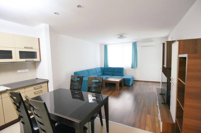 Obývací pokoj s modrou sedačkou, kuchyní a podlahou s dřevěným dekorem v 2-pokojovém bytě.