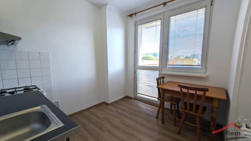 Kuchyně v 1-pokojovém bytě s podlahou s dřevěným dekorem, dřezem, stolem a židlemi.