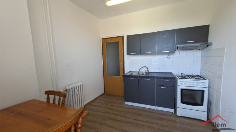 Kuchyně s šedou linkou a dřevěným stolem v 1-pokojovém bytě, podlaha s dřevěným dekorem.