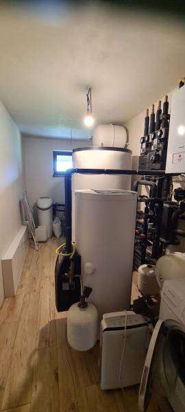 Technická místnost v rodinném domě s kotlem, nádržemi a podlahou s dřevěným dekorem.