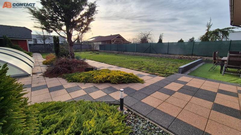 Zahrada u rodinného domu na Větrné ulici v Krakovanech s dlažbou a terasou.
