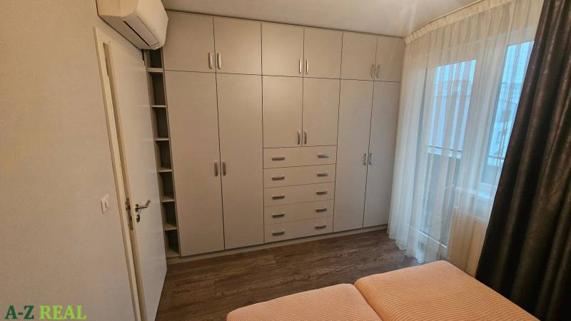 Ložnice s bílou vestavěnou skříní a postelí ve 3pokojovém bytě s podlahou s dřevěným dekorem.