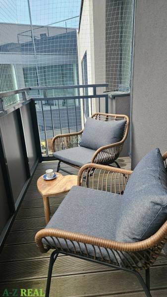 Balkon s pohodlnými křesly a stolkem ve 3-pokojovém bytě s podlahou s dřevěným dekorem.