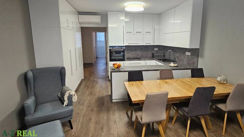 Kuchyně v 3pokojovém bytě s podlahou s dřevěným dekorem, jídelním stolem a světlým nábytkem.