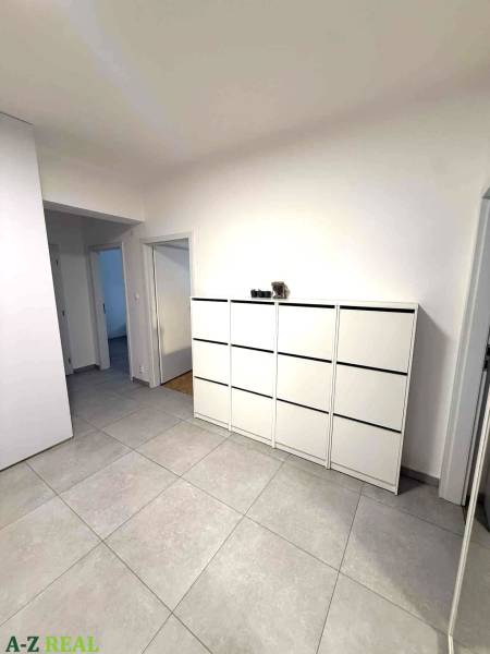 Prostorná chodba se světlými dlaždicemi a bílou komodou ve 4pokojovém bytě.