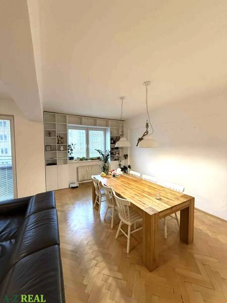 Jídelní stůl ve čtyřpokojovém bytě s podlahou s dřevěným dekorem a bílými židlemi.