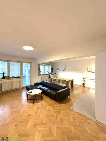 Obývací pokoj ve 4pokojovém bytě s podlahou s dřevěným dekorem a černou pohovkou.