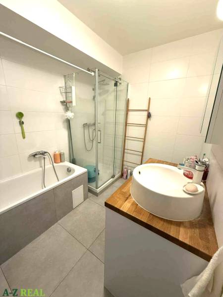 Koupelna s vanou, sprchovým koutem a umyvadlem na dřevěné desce ve 4-pokojovém bytě.