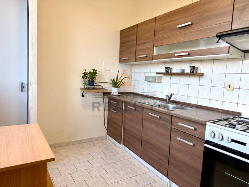 Kuchyně s linkou a sporákem v 1-pokojovém bytě, světlé dlaždice, dřevěný dekor.