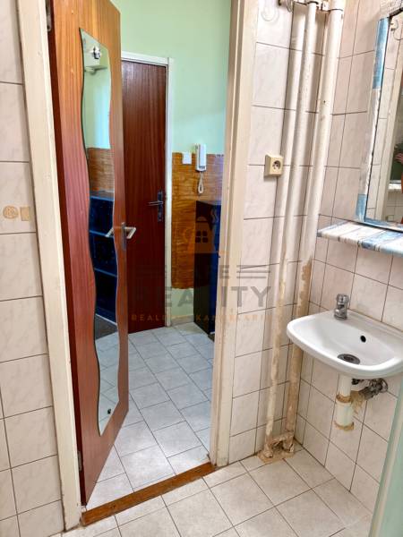 Koupelna v 1-pokojovém bytě se zrcadlem, umyvadlem a bílými obkladačkami.