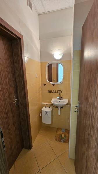 Koupelna v obchodních prostorách s umyvadlem a zrcadlem, obložená světlými kachličkami.