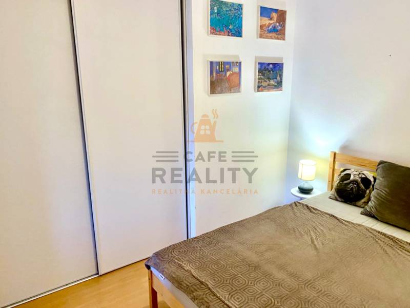 Ložnice v dvoupokojovém bytě s postelí, vestavěnou skříní a dekoracemi na stěně.