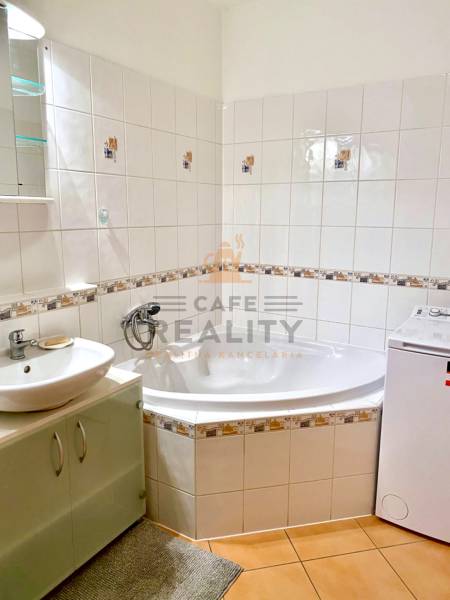 Koupelna s dlažbou, vanou a pračkou v 2-pokojovém bytě.