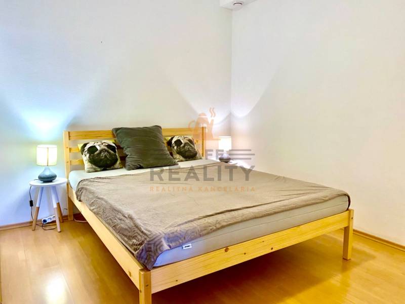 Ložnice v dvoupokojovém bytě s dřevěným dekorem a polštáři na posteli.