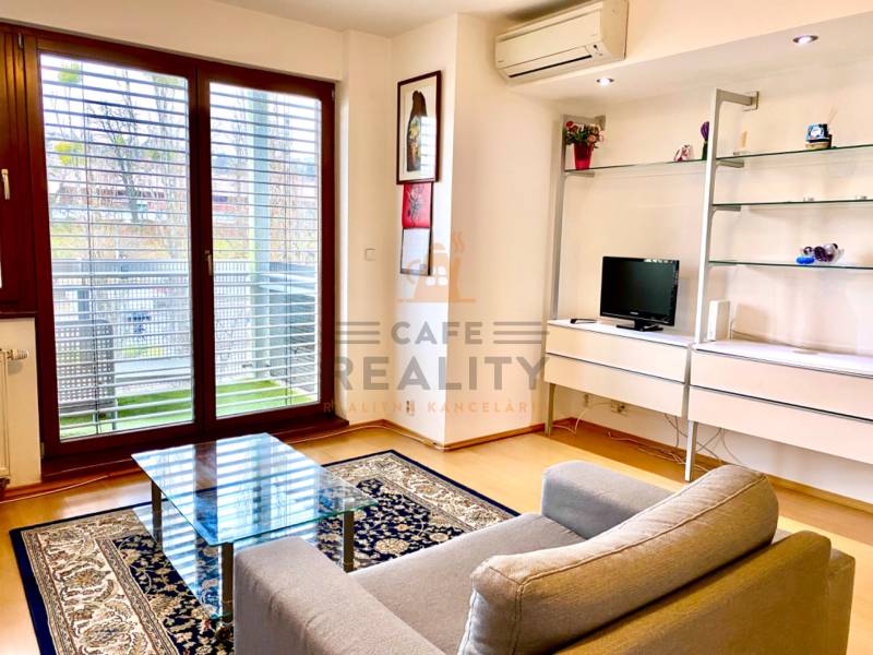 Obývací pokoj v 2-pokojovém bytě s křeslem, skleněným stolem a podlahou s dřevěným dekorem.