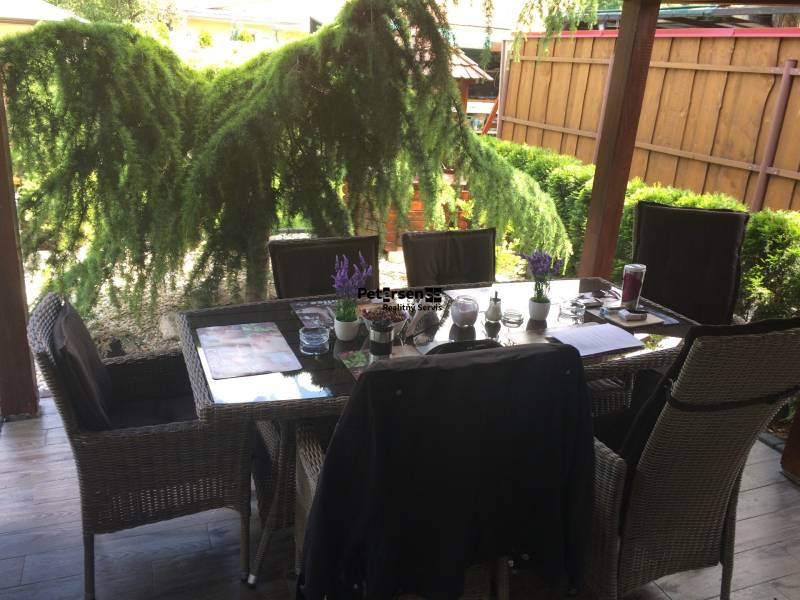 Rodinný dům s posezením na terase, včetně podlahy s dřevěným dekorem a zahradní zeleně.