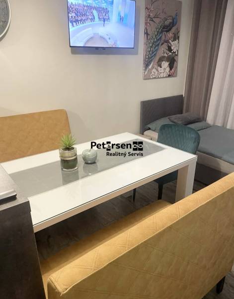 Obývací část s TV v rodinném domě, skleněný stůl, pohovky, obraz páva, podlaha s dřevěným dekorem.