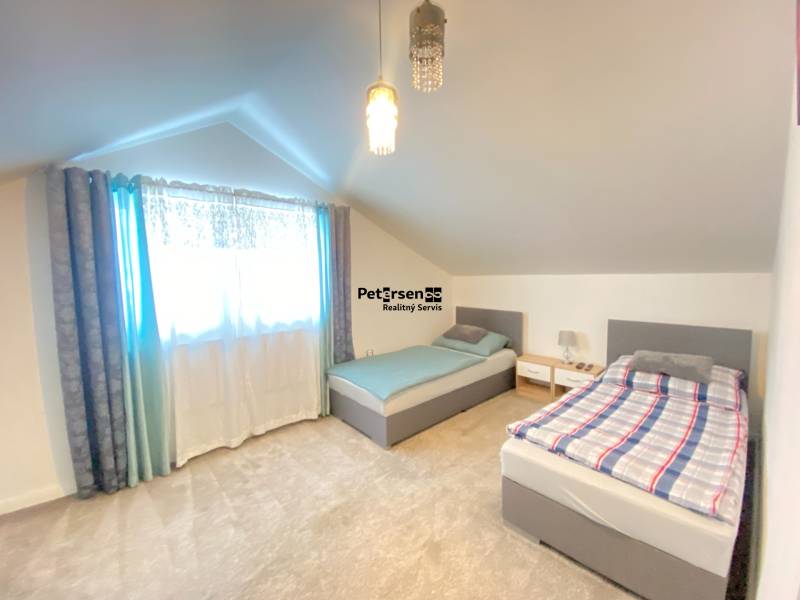 Podkrovní pokoj se dvěma postelemi a jemným kobercem v rodinném domě.