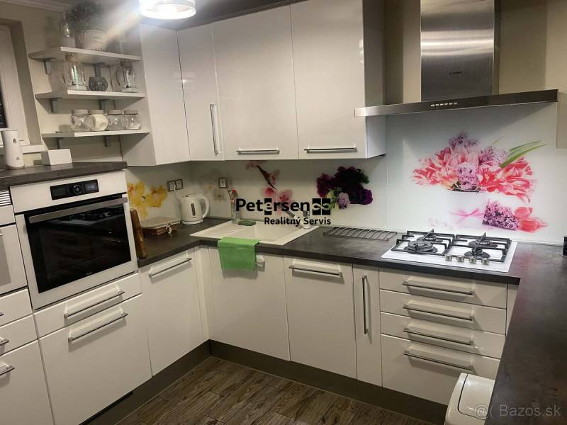 Kuchyně v rodinném domě s bílými skříňkami, dekorativním obkladem a podlahou s dřevěným dekorem.