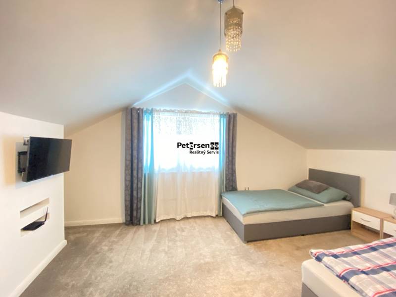 Ložnice v rodinném domě se dvěma postelemi, televizí a kobercovou podlahou.