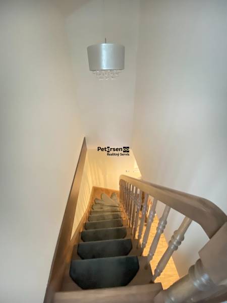 Schodiště s kobercem vede nahoru, nad ním visí svítidlo v rodinném domě.