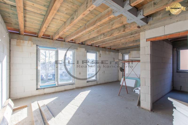 Interiér rozestavěné budovy s dřevěným stropem a velkými okny.