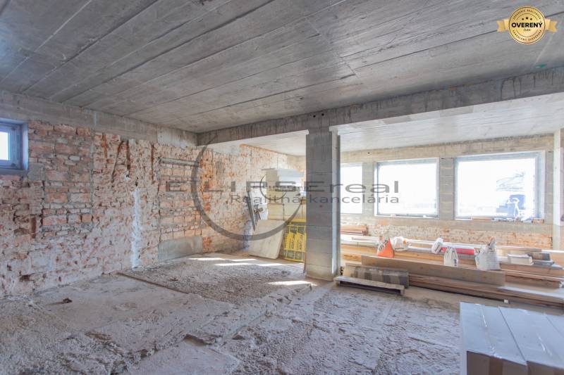 Staveniště v budově s cihlovými stěnami a velkými okny. Stavba je ve fázi výstavby.