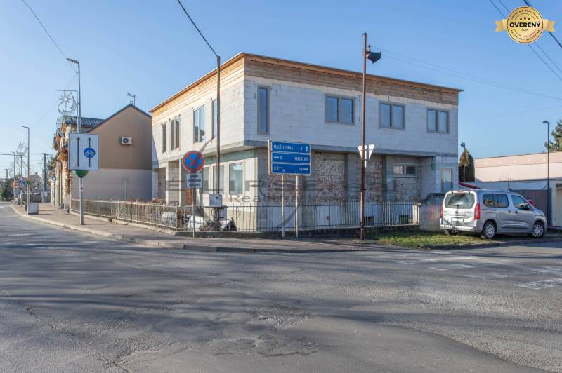 Budova ve Velkých Levárech, u cesty, s zaparkovaným autem a dopravními značkami.