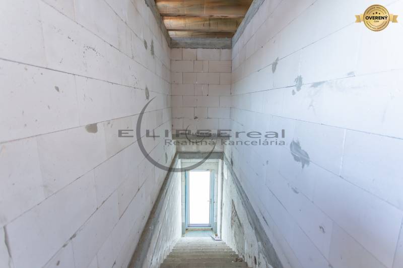 Pohled na schodiště v budově s betonovými stěnami a oknem na konci.