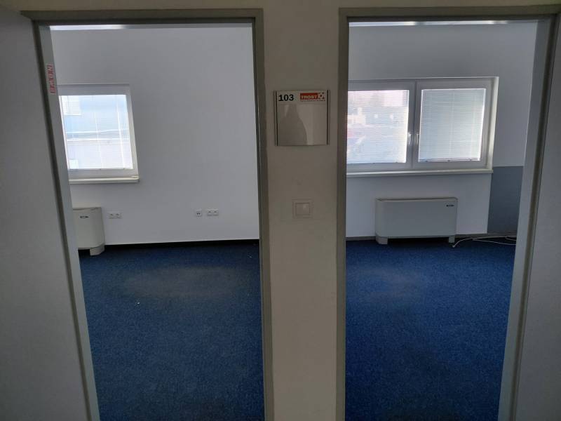 Interiér kanceláří s modrým kobercem a okny s roletami.