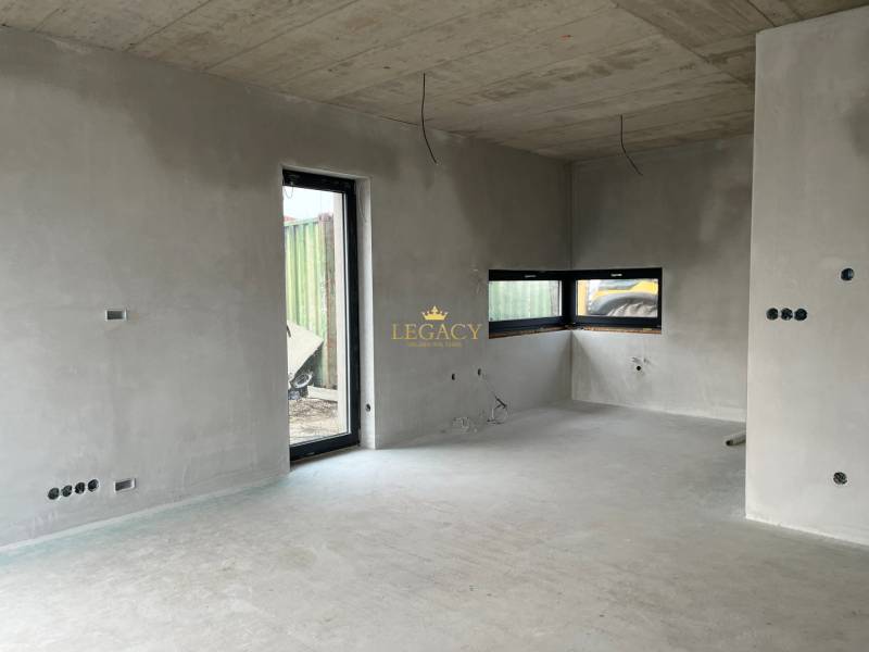 Interiér rodinného domu s betonovými stěnami a velkými okny, vidět neúplnou elektrickou instalaci.