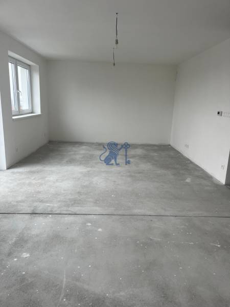 Prázdná místnost v 3-pokojovém bytě s betonovou podlahou a oknem.