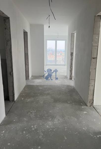 Chodba v 3-pokojovém bytě, bílé stěny, velké okno, podlaha bez povrchové úpravy.